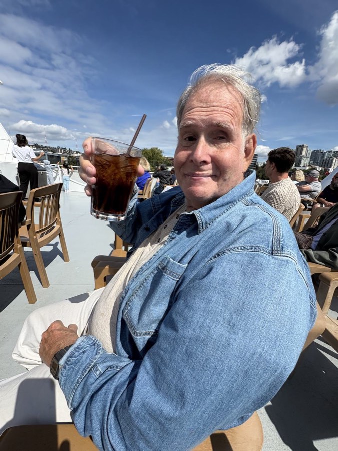 Norman on the top deck of a harbour cruise boat, holding up a glass of Coke